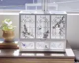 Boîte à bijoux ornée de vitraux décoratifs représentant des papillons et des fleurs, posée sur une commode en bois.