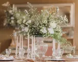 Un bouquet de vitrail fleur, blanc et aérien, orne une table dressée avec des bougies et des verres délicats.