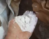 Main d'une personne tenant une poudre blanche fine, de la chaux morte, sortant d'un sac en papier.