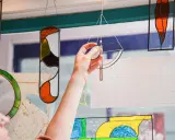 Une main ajuste un vitrail coloré, œuvre d'un fabricant de vitraux, devant une fenêtre.
