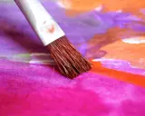 Pinceau humide sur une toile aux couleurs vives, mélangeant le pastel sec et l'eau pour créer des dégradés vibrants de rose, violet et orange.