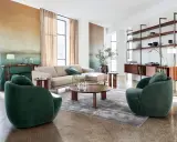 Salon au style mid century avec canapé beige, fauteuils verts velours, table basse ronde en bois et étagères murales.