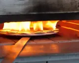 Des pièces de métal attendent d'être émaillées dans un four, sous des flammes vives. L'artisan émailleur surveille attentivement la cuisson.