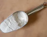Une pelle métallique remplie de poudre blanche, peut-être de la colle gomme arabique, sur un fond texturé.