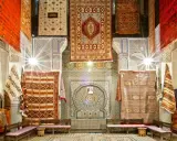 Un intérieur richement décoré de tapis colorés, témoignant de l'artisanat de Fès. Des motifs géométriques et floraux ornent les murs et les sols.