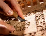 Main d'artisan sculptant un détail floral sur un meuble en bois, étape clé pour savoir comment nettoyer un meuble en marqueterie.