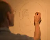 Un artiste esquisse un dessin vitraux, le visage de Jésus prenant forme sous son crayon.