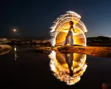 Une femme en robe blanche danse sous un ciel étoilé, entourée d'un halo de lumière incandescente, comme un **verre soleil** reflété dans l'eau.