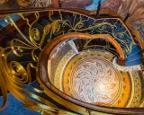 Escalier en colimaçon orné d'une rampe dorée aux volutes végétales, rappelant une fleur art nouveau. Le sol en mosaïque circulaire est un chef-d'œuvre.