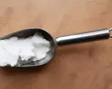 Une cuillère métallique contient une pâte blanche, peut-être de la cire saponifiée sur enduit chaux, prête à être appliquée.