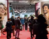 Foule dans un salon, devant de grandes affiches publicitaires. L'esprit meuble est palpable, les gens déambulent, curieux.