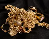 Un amas de bijoux en or, chaînes et bagues, sur fond noir. Pour savoir comment reconnaître de l'or sur une pierre, observez sa couleur et son éclat.