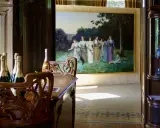 Bouteilles de champagne sur une table en bois sculpté, devant une peinture de femmes dans un jardin, ambiance Villa Mademoiselle Reims.