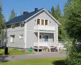 Maison à deux étages avec une peinture suédoise blanche, un balcon, une porte bleue et un jardin verdoyant.