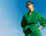 Une femme en tenue verte éclatante, lunettes de soleil futuristes, pose sous un ciel bleu. Un **cahier de tendance** inspirant.