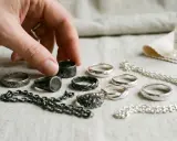 Maintenant, je sais avec quoi nettoyer de l'argent : une main choisit une bague parmi plusieurs, à côté d'une bouteille de nettoyant pour argent.