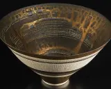Vase texturé aux reflets dorés et noirs, œuvre d'un céramiste connu, évoquant une cité futuriste.