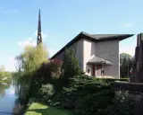 L'église Saint-Rémy de Baccarat, avec sa flèche élancée, se dresse près d'une rivière bordée d'arbres verdoyants.