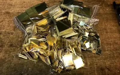 Des petits carrés de laiton brillants, prêts pour un projet de comment décaper du laiton. Ils sont dans des sacs en plastique sur une table en bois.