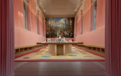 Installation d'art contemporain à Venise, évoquant le *homo faber*. Un tapis coloré et une table ornée de sculptures sous un grand tableau.