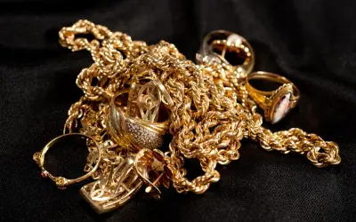 Un amas de bijoux en or, chaînes et bagues, sur fond noir. Pour savoir comment reconnaître de l'or sur une pierre, observez sa couleur et son éclat.