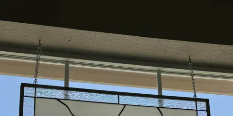 Comment fixer un vitrail sur une fenêtre : un panneau de verre bleu et blanc est suspendu par des chaînes à des crochets fixés au plafond.