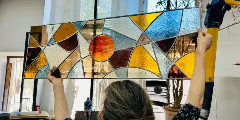 Un artiste admire son œuvre, un vitrail aux couleurs chaudes et géométriques, fruit d'un cours de vitrail.