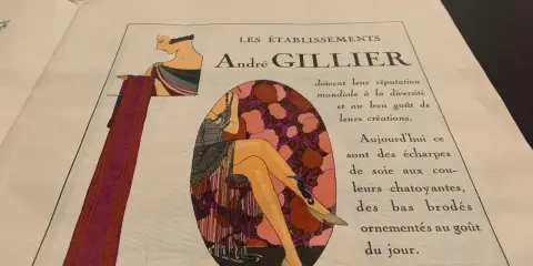 Publicité André Gillier, style art déco, avec une femme aux jambes ornées de bas brodés, rappelant les dates de cette époque.