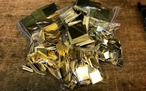 Des petits carrés de laiton brillants, prêts pour un projet de comment décaper du laiton. Ils sont dans des sacs en plastique sur une table en bois.