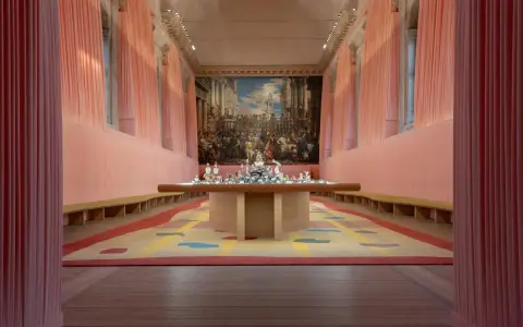 Installation d'art contemporain à Venise, évoquant le *homo faber*. Un tapis coloré et une table ornée de sculptures sous un grand tableau.