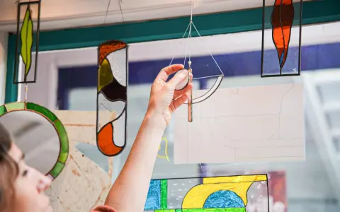 Une main ajuste un vitrail coloré, œuvre d'un fabricant de vitraux, devant une fenêtre.
