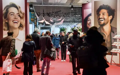 Foule dans un salon, devant de grandes affiches publicitaires. L'esprit meuble est palpable, les gens déambulent, curieux.