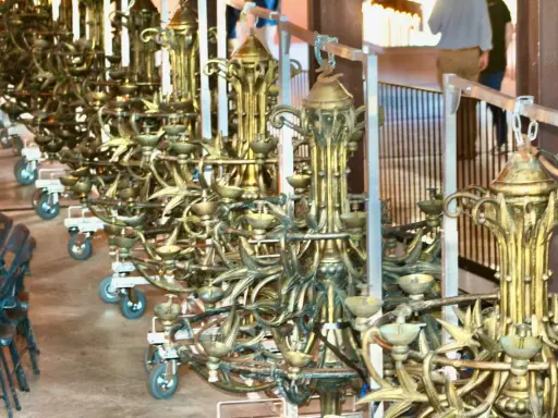 Une rangée de grands candélabres dorés, prêts pour un événement. Ce lustrier métier, complexe et orné, attend d'illuminer la scène.