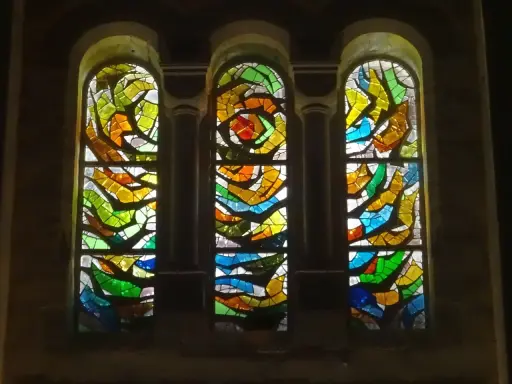 Trois vitraux aux formes abstraites et aux couleurs vives, un exemple de comment éclairer un vitrail pour révéler sa beauté.