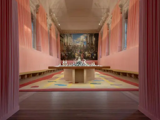 Installation d'art contemporain à Venise, évoquant le *homo faber*. Un tapis coloré et une table ornée de sculptures sous un grand tableau.