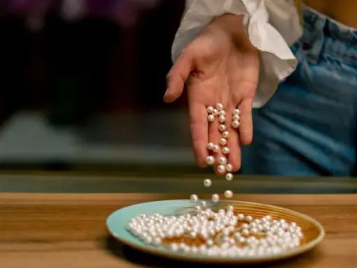 Main d'une personne versant des perles de culture sur une assiette. Apprenez comment nettoyer les perles de culture pour qu'elles brillent.