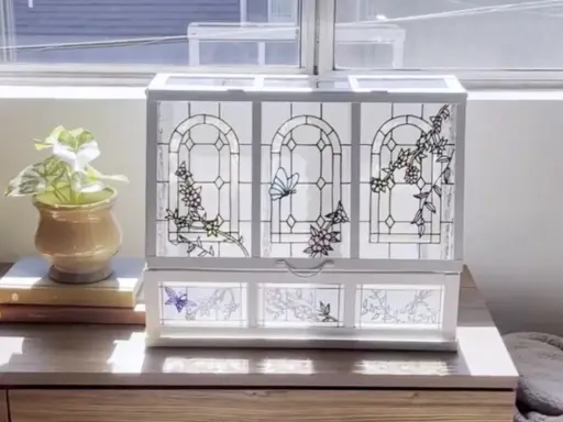 Boîte à bijoux ornée de vitraux décoratifs représentant des papillons et des fleurs, posée sur une commode en bois.
