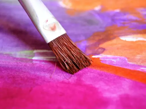 Pinceau humide sur une toile aux couleurs vives, mélangeant le pastel sec et l'eau pour créer des dégradés vibrants de rose, violet et orange.