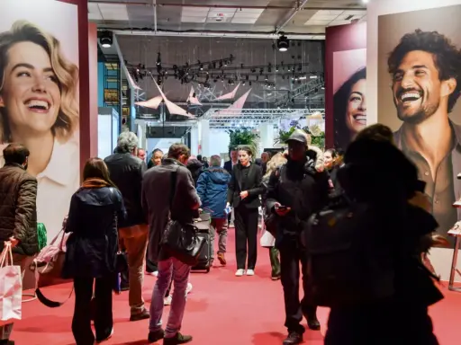 Foule dans un salon, devant de grandes affiches publicitaires. L'esprit meuble est palpable, les gens déambulent, curieux.