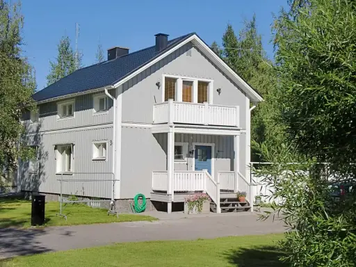 Maison à deux étages avec une peinture suédoise blanche, un balcon, une porte bleue et un jardin verdoyant.