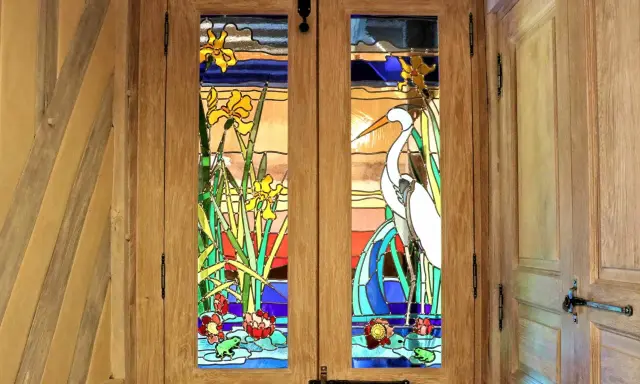 Portes en bois ornées de vitraux représentant des iris, un héron et des nénuphars. L'art de faire des vitraux sublime cette entrée.