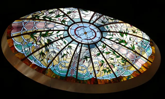 Magnifique vitrail intérieur maison, orné de fleurs roses et de motifs végétaux bleus et jaunes, illuminant la pièce.