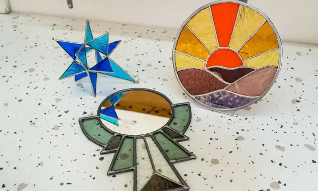 Trois pièces d'art en vitrail : une étoile bleue, un soleil couchant et un miroir ornemental. Créations d'un atelier vitrail Paris.