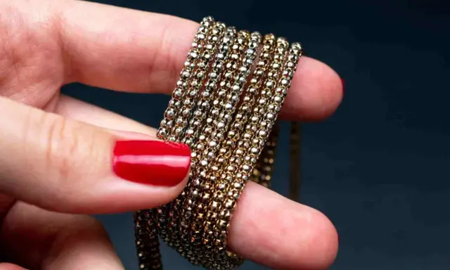 Main d'une femme aux ongles rouges tenant une chaîne de métal doré, montrant comment nettoyer métal doré noirci.