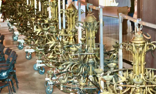Une rangée de grands candélabres dorés, prêts pour un événement. Ce lustrier métier, complexe et orné, attend d'illuminer la scène.
