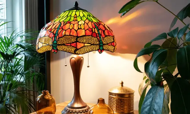 Lampe tiffany origine, abat-jour en vitrail coloré avec libellules, sur une table en bois avec des plantes.
