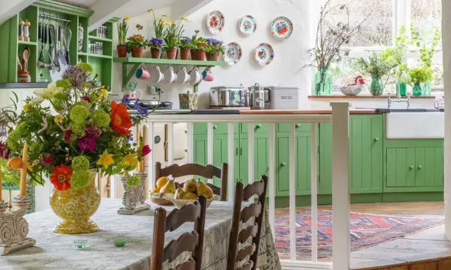 Cuisine lumineuse avec armoires vertes, bouquet de fleurs coloré sur la table, et vaisselle décorative. Ambiance chaleureuse de deco cottage chic.