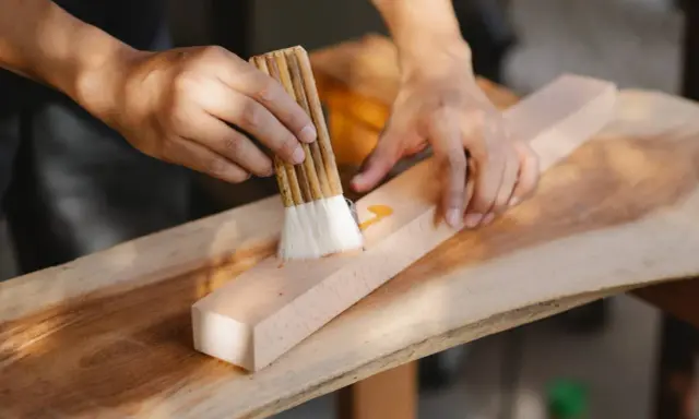Un artisan ébéniste applique une finition sur un morceau de bois avec un pinceau.