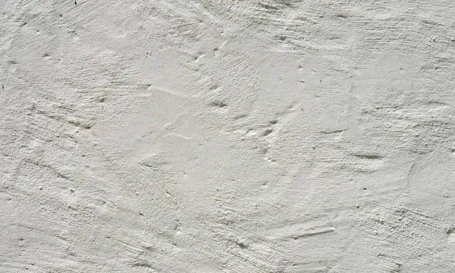 Texture d'enduit à la chaux blanc, présentant des irrégularités et des taches subtiles, témoignant de son application manuelle.