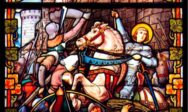 Vitrail de Jeanne d'Arc, la Pucelle d'Orléans, en armure sur son cheval blanc, brandissant son épée au milieu d'une bataille.
